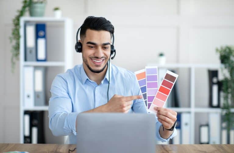 Arab man holding color swatches in front of laptop at office, presenting graphic design project