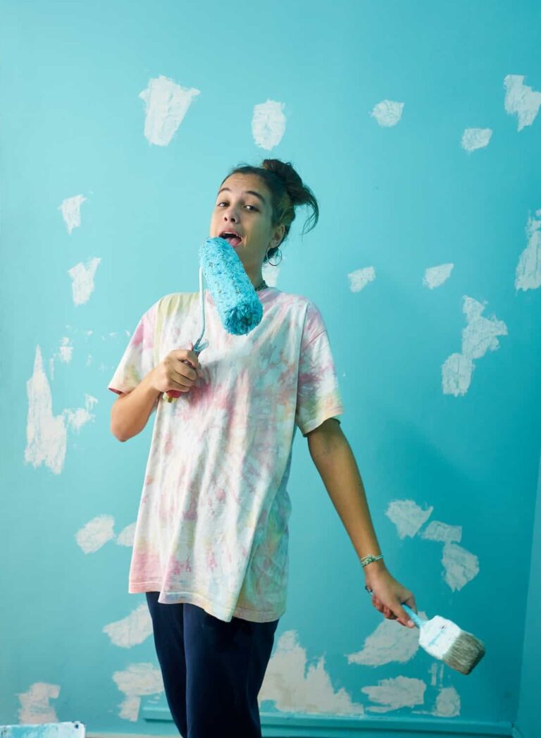 happy woman painting interior wall with paint roller in new house