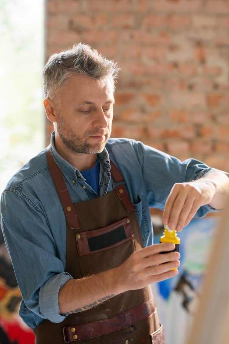 Mature painter in workwear uncovering plastic jar with gouache