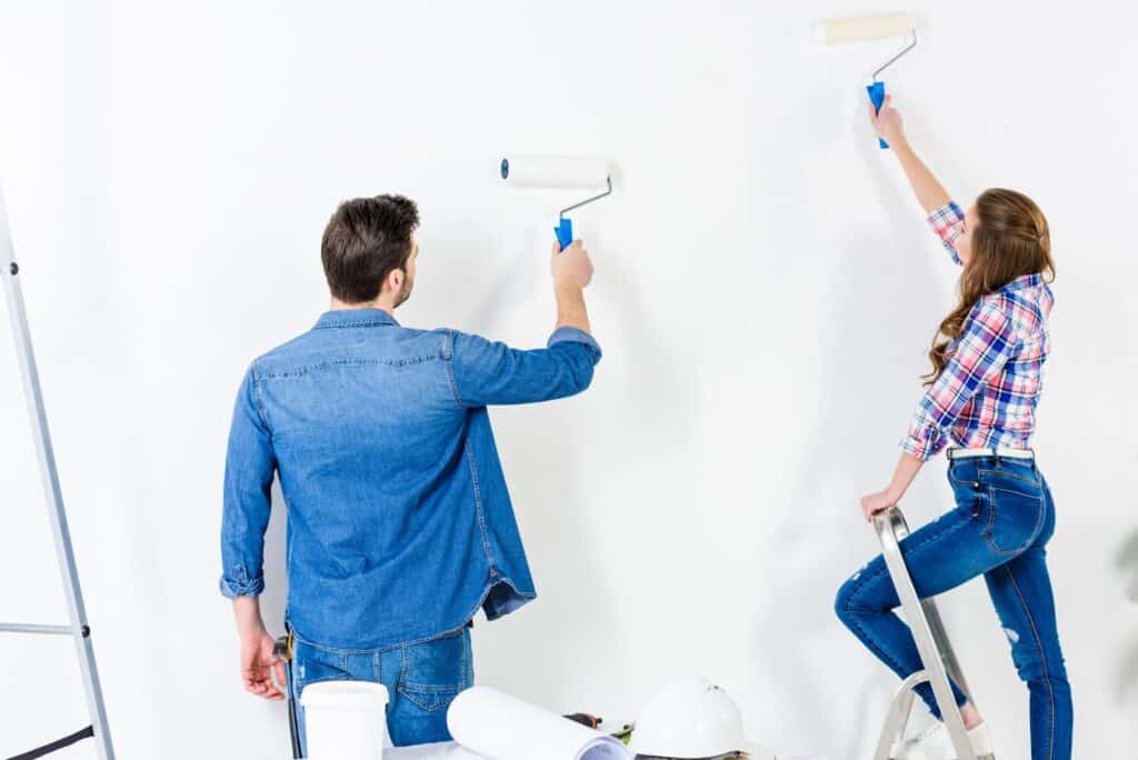 rear view of couple painting wall with white paint